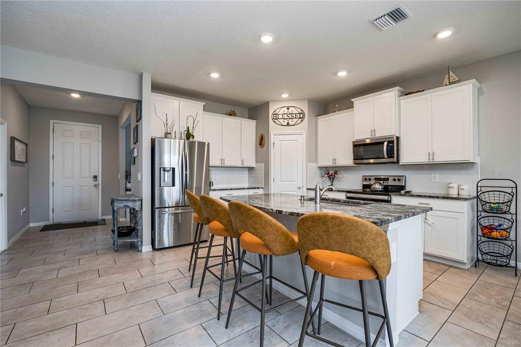 A kitchen features white cabinets, granite countertops, an island with three stools, and tile flooring — 5329 HALEWOOD COURT, BRADENTON, FL