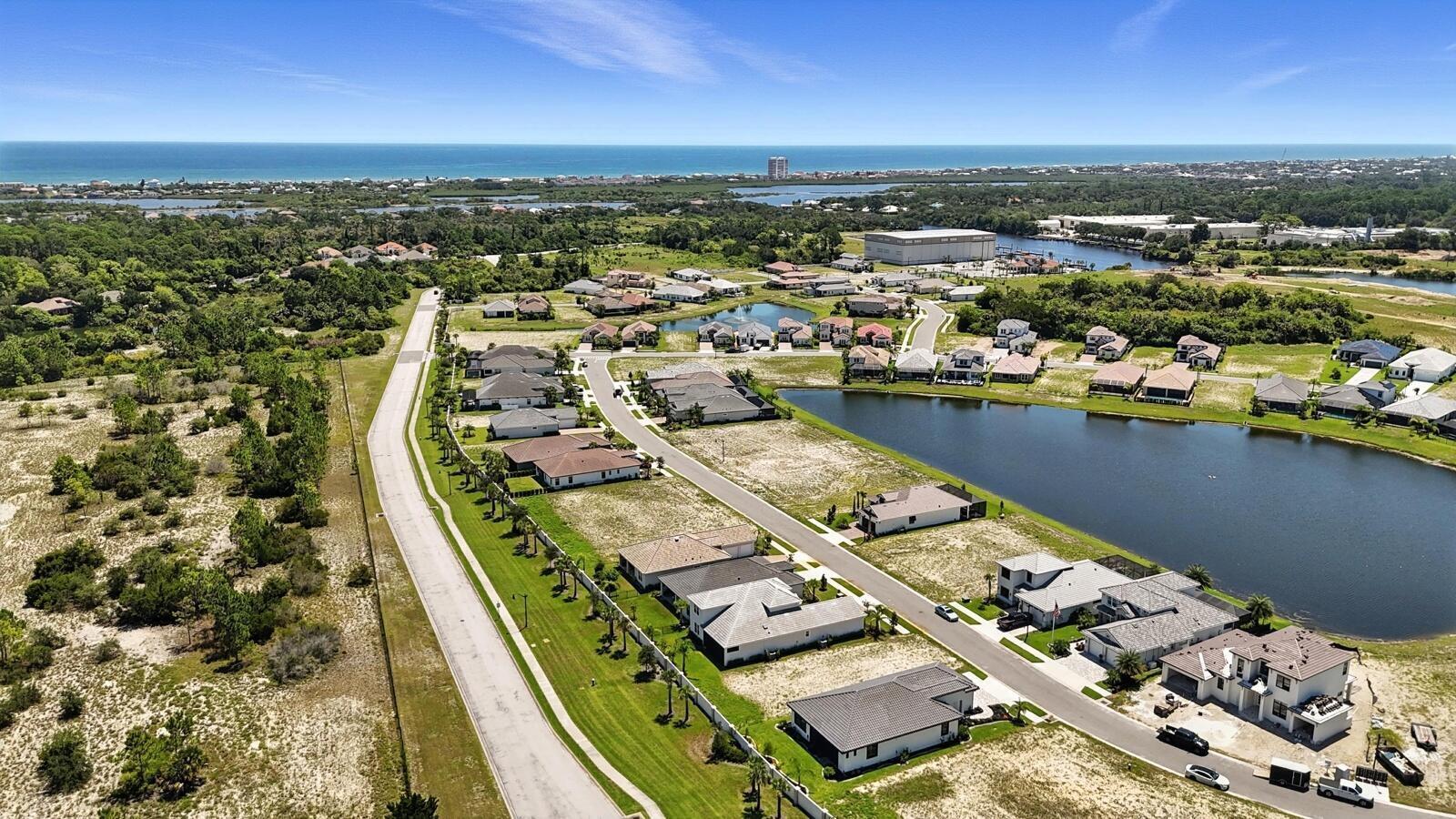 An aerial view shows a suburban neighborhood with houses, a lake, and coastal scenery — 27 Del Palma Drive, Palm Coast FL 32137, PALM COAST, FL