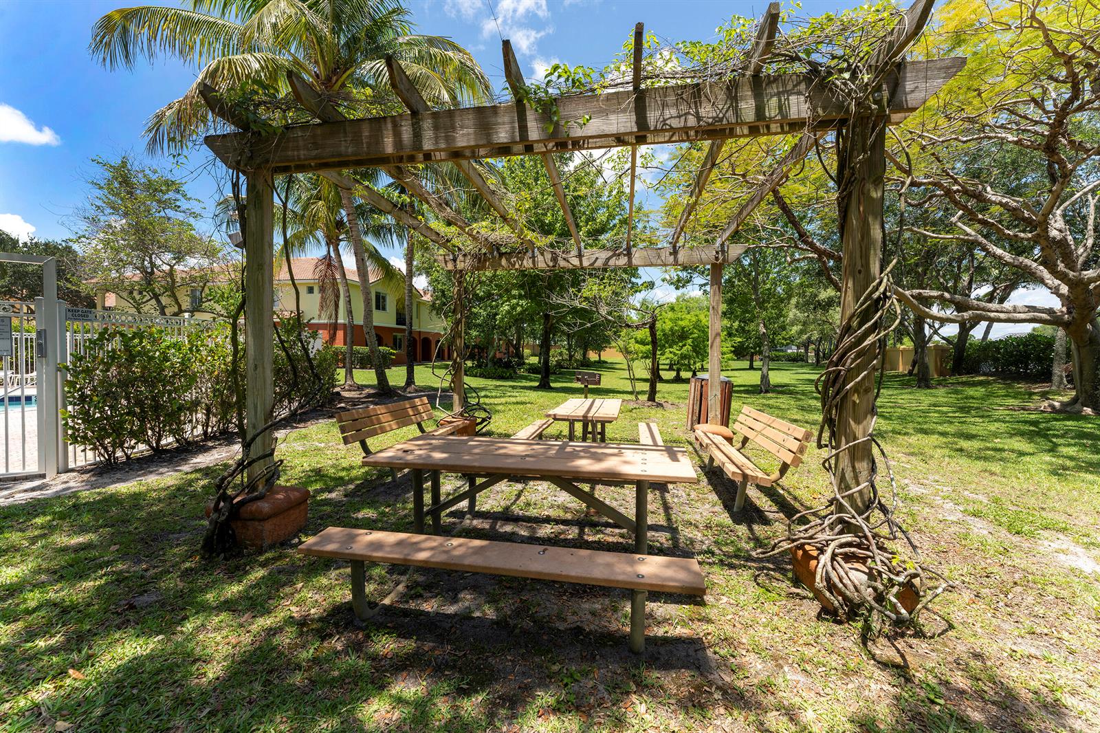 A wooden pergola covers a picnic table and benches in a grassy outdoor park area — 49 SE Sedona Circle # 101, Stuart FL 34994, STUART, FL