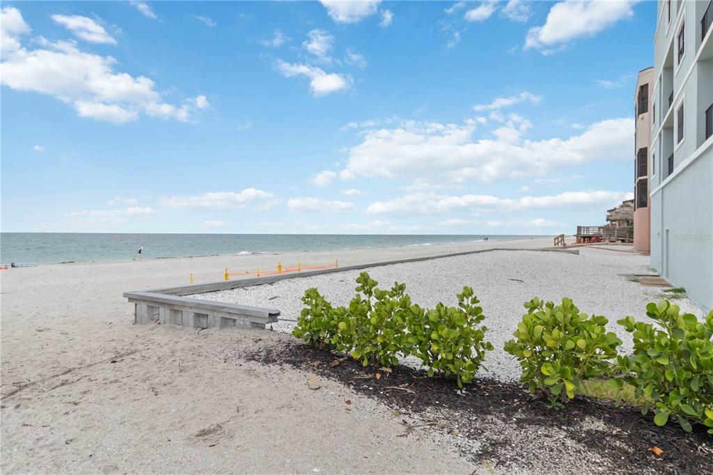 A view of a sandy beach next to a building with a landscaped garden area — 50 MEREDITH DRIVE UNIT 8, ENGLEWOOD, FL