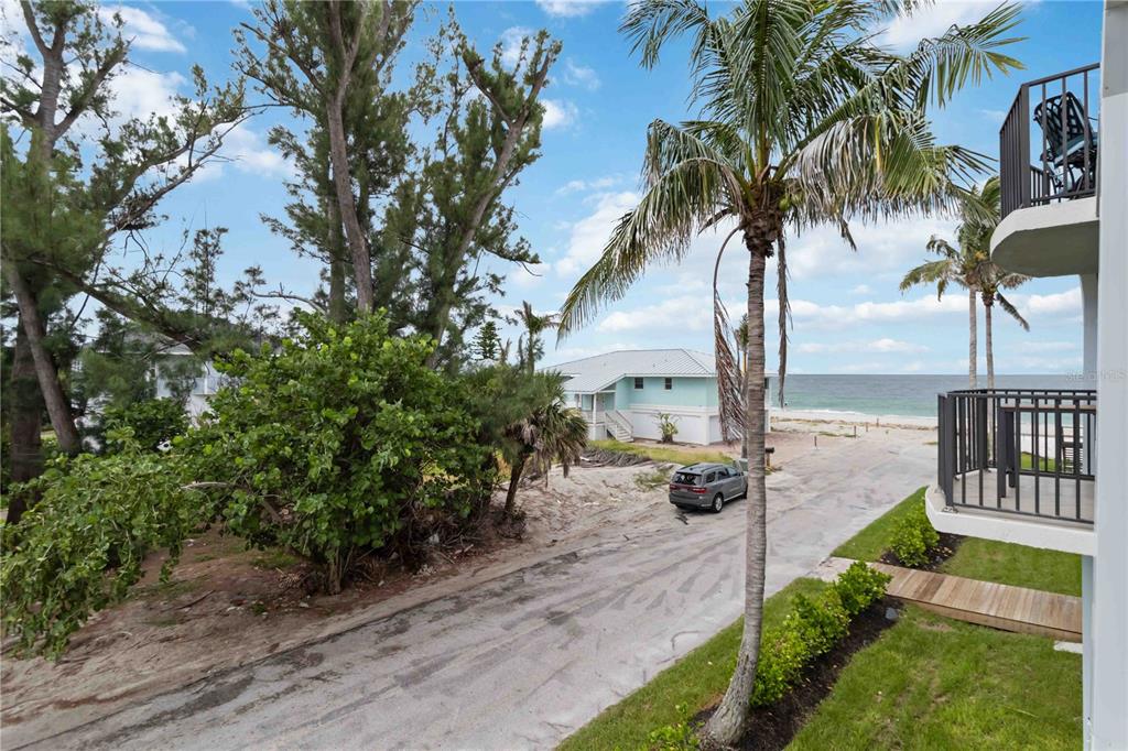 An exterior view of a beachside property featuring a paved driveway, palm trees, and ocean — 50 MEREDITH DRIVE UNIT 8, ENGLEWOOD, FL