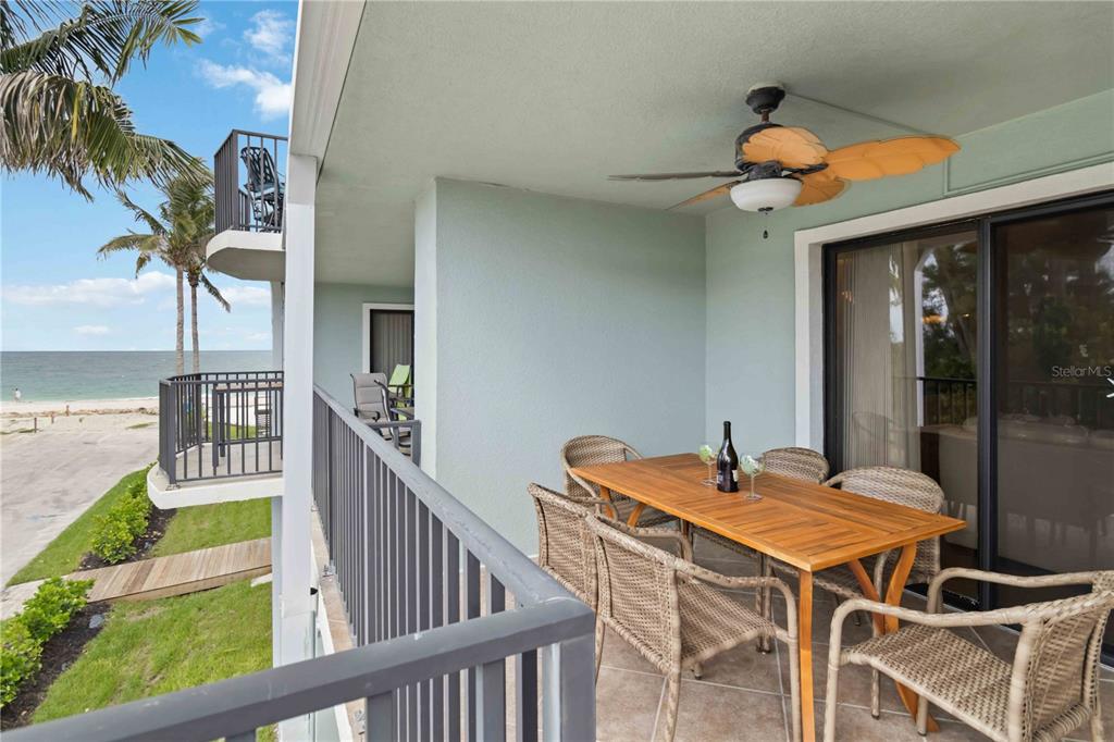 A balcony features a wooden dining table, wicker chairs, a ceiling fan, and ocean views — 50 MEREDITH DRIVE UNIT 8, ENGLEWOOD, FL