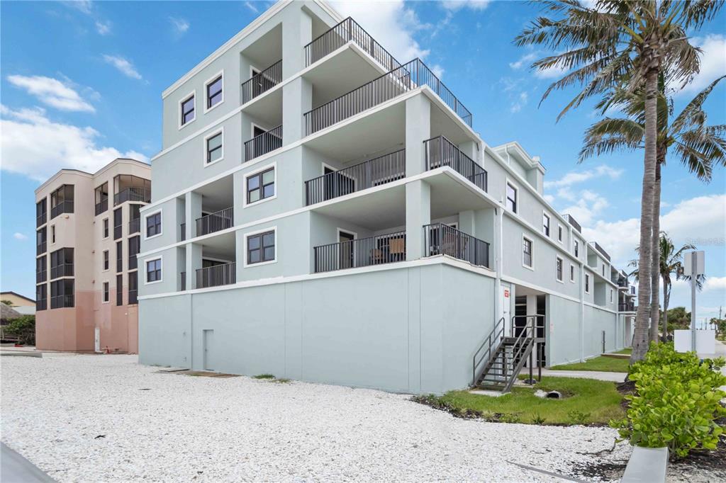 A multi-story, light blue residential building with balconies and a gravel parking area — 50 MEREDITH DRIVE UNIT 8, ENGLEWOOD, FL