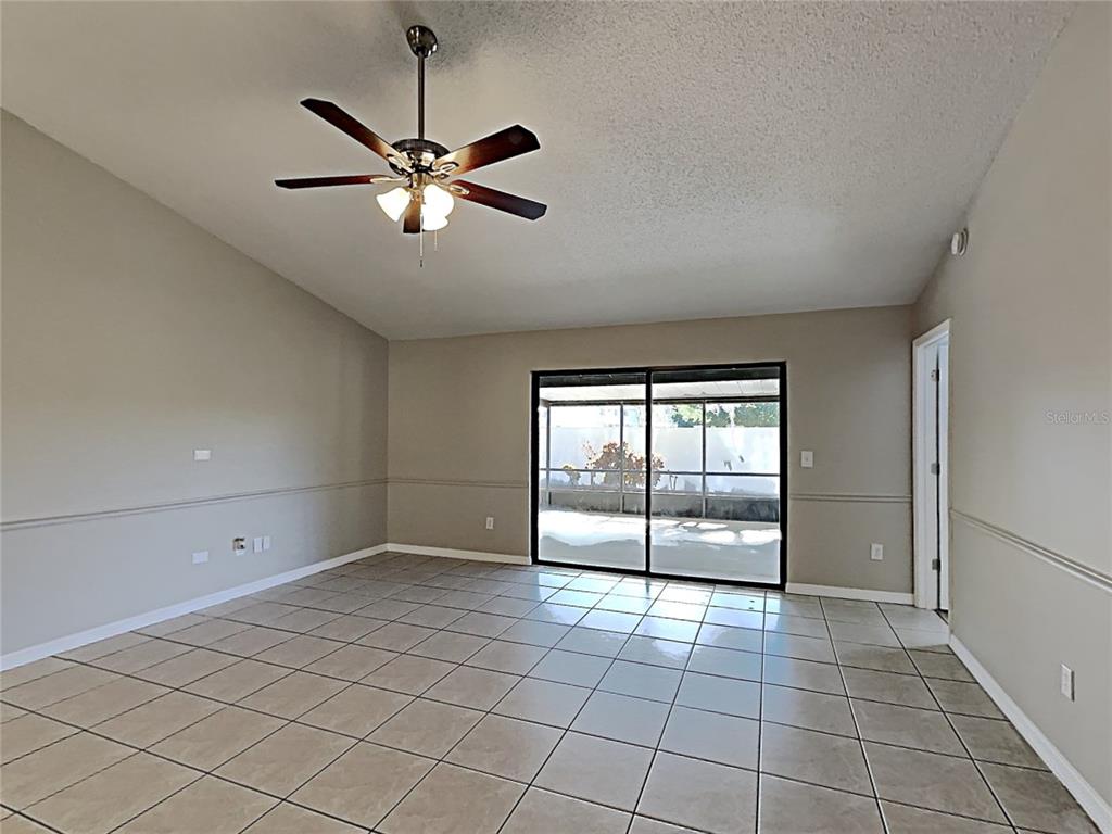 An empty room with beige walls, tile flooring, a ceiling fan, and sliding glass doors — 11701 LYNMOOR DRIVE, RIVERVIEW, FL