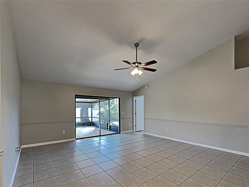 A living room with beige walls, tile flooring, a ceiling fan, and a sliding glass door — 11701 LYNMOOR DRIVE, RIVERVIEW, FL