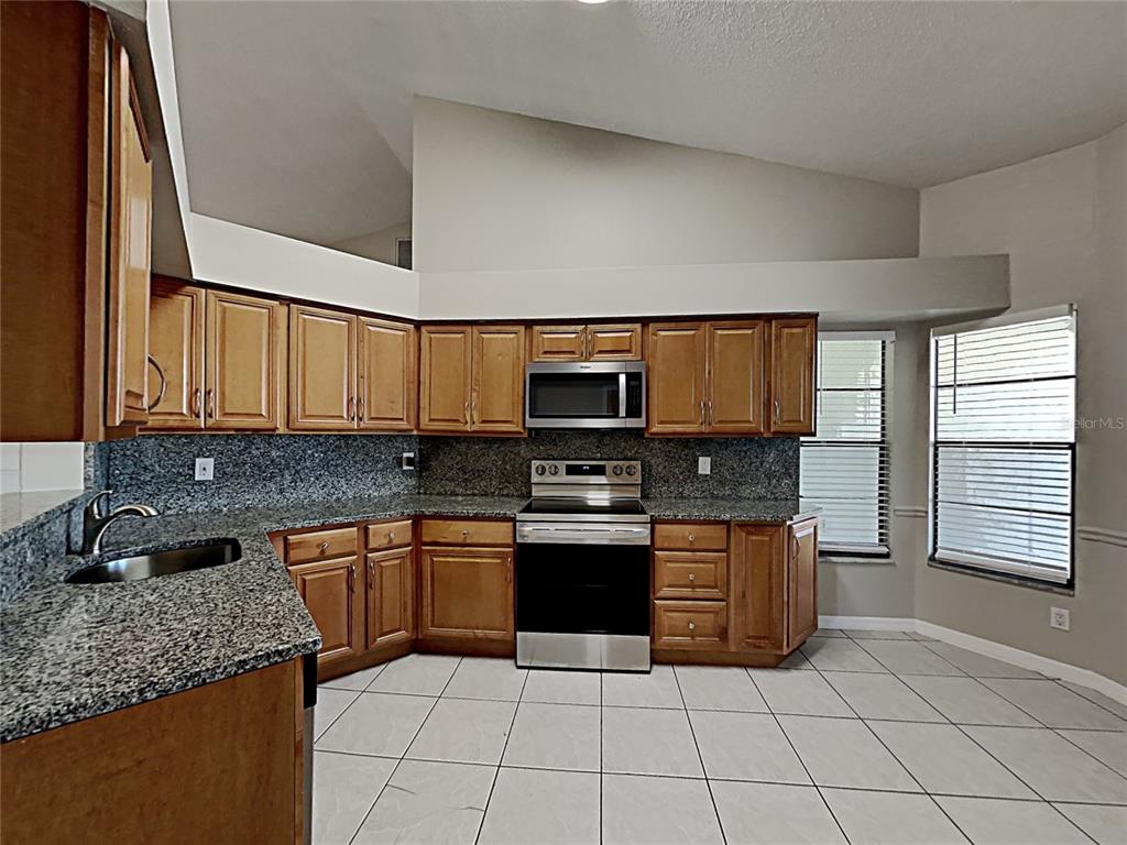 A kitchen features wood cabinets, granite countertops, stainless steel appliances, and white tile flooring — 11701 LYNMOOR DRIVE, RIVERVIEW, FL