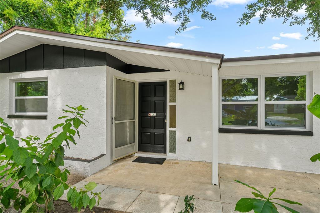 The exterior of a white house features a black front door and a concrete porch — 1651 ATLAS LANE, HOLIDAY, FL