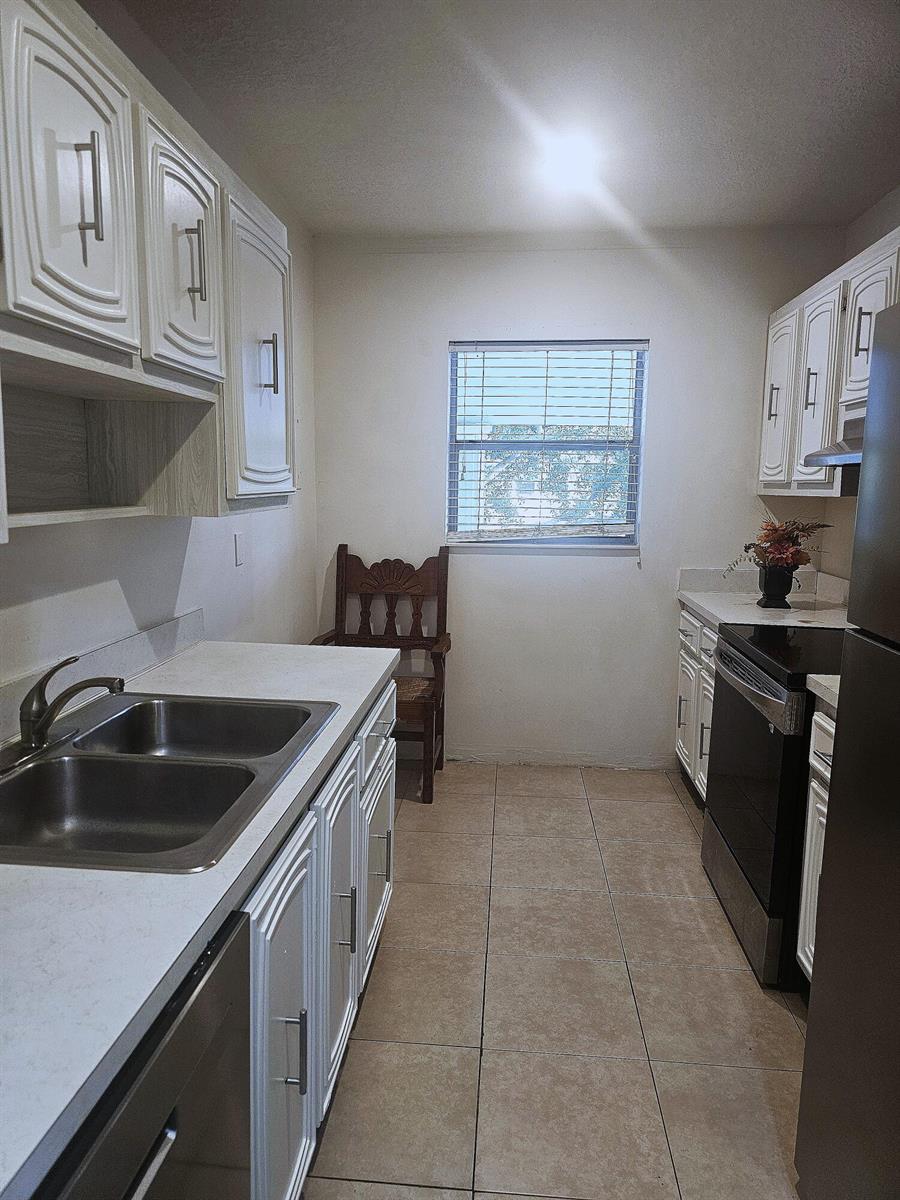 A galley kitchen features white cabinets, stainless steel appliances, light countertops, and beige tile flooring — 2600 SW 22nd Avenue # 908, Delray Beach FL 33445, DELRAY BEACH, FL