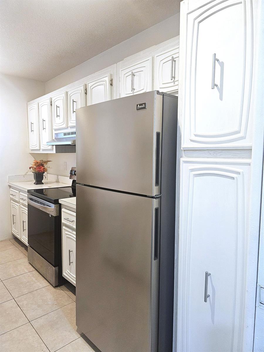 A kitchen features white cabinetry, stainless steel appliances, and light-colored tile flooring — 2600 SW 22nd Avenue # 908, Delray Beach FL 33445, DELRAY BEACH, FL