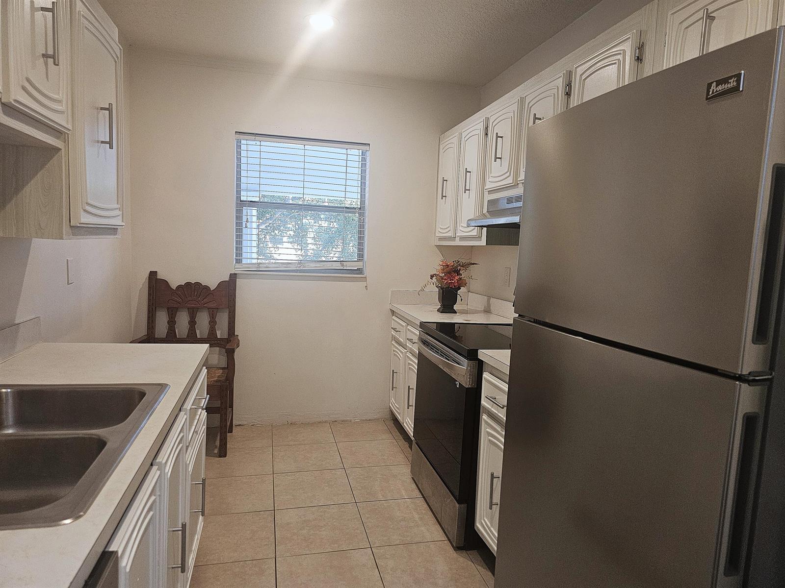 A galley kitchen features white cabinets, stainless steel appliances, and light-colored tile flooring — 2600 SW 22nd Avenue # 908, Delray Beach FL 33445, DELRAY BEACH, FL