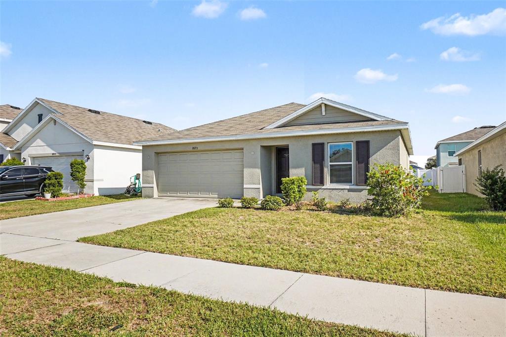A single-story suburban house with a beige stucco exterior, a two-car garage, and a lawn — 10213 CLOUDBURST COURT, RIVERVIEW, FL