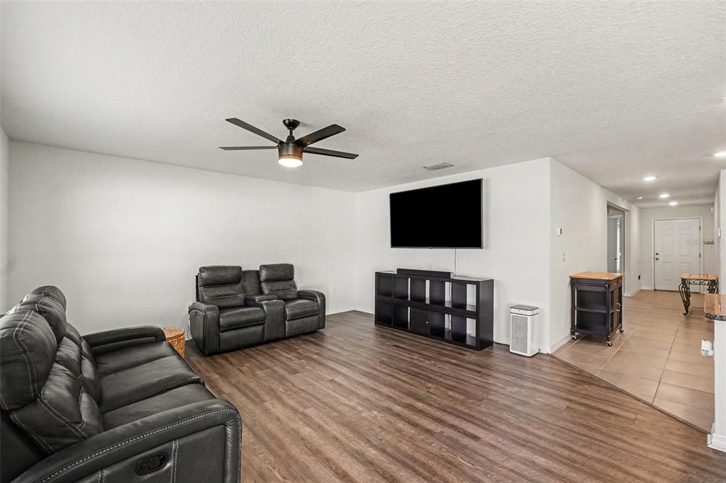 A living room features dark leather furniture, a wall-mounted television, and wood-look flooring — 10213 CLOUDBURST COURT, RIVERVIEW, FL