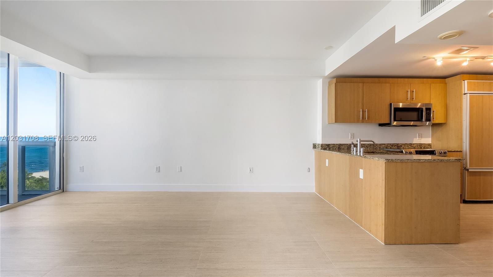 An open-concept living area features light wood flooring, a kitchen with wood cabinets, and ocean views — 10275 Collins Ave # 905, Bal Harbour FL 33154, BAL HARBOUR, FL