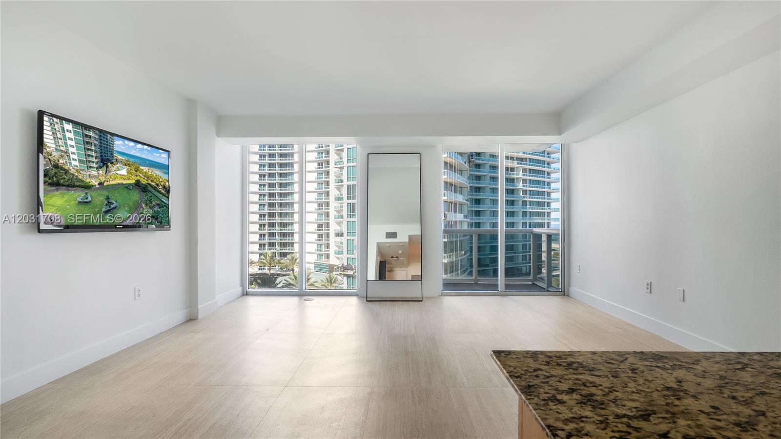 A bright living area features light wood-look flooring, a wall-mounted television, and floor-to-ceiling windows — 10275 Collins Ave # 905, Bal Harbour FL 33154, BAL HARBOUR, FL