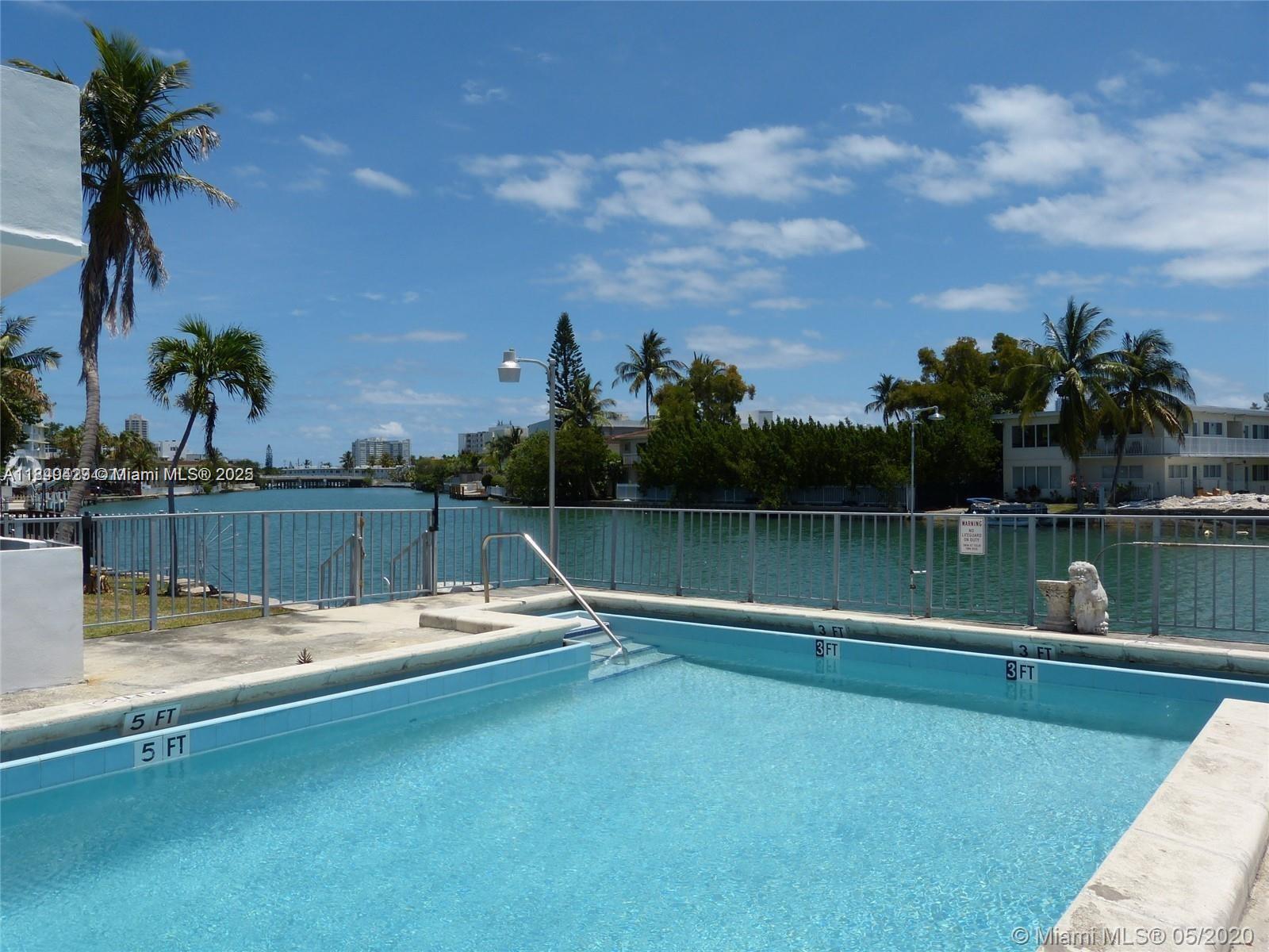 A swimming pool overlooks a canal with palm trees and buildings in the background — 250 S Shore Dr # 5, Miami Beach FL 33141, MIAMI BEACH, FL