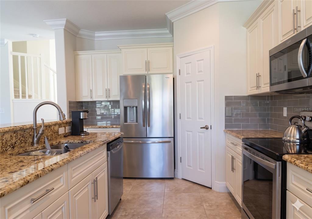 A kitchen features stainless steel appliances, granite countertops, off-white cabinetry, and a gray tile backsplash — 11483 BEACON POINTE LANE, WELLINGTON, FL