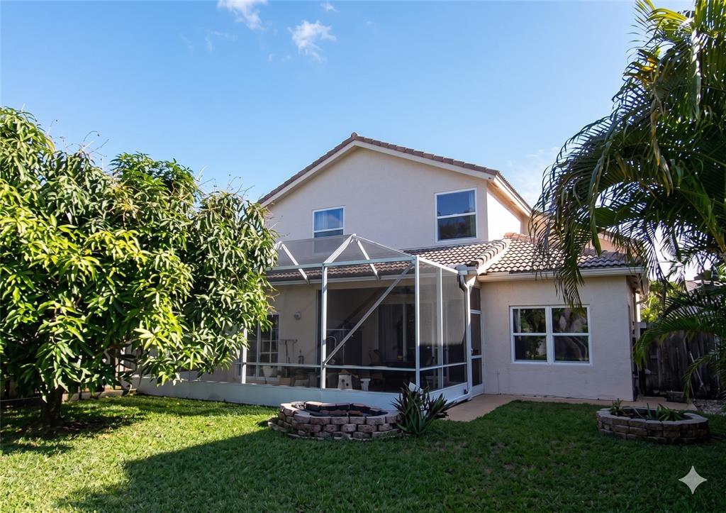 The backyard features a screened-in patio, a stone fire pit, and a large mango tree — 11483 BEACON POINTE LANE, WELLINGTON, FL