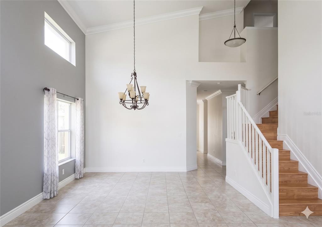 A high-ceilinged dining area features tile flooring, a chandelier, and a wooden staircase — 11483 BEACON POINTE LANE, WELLINGTON, FL