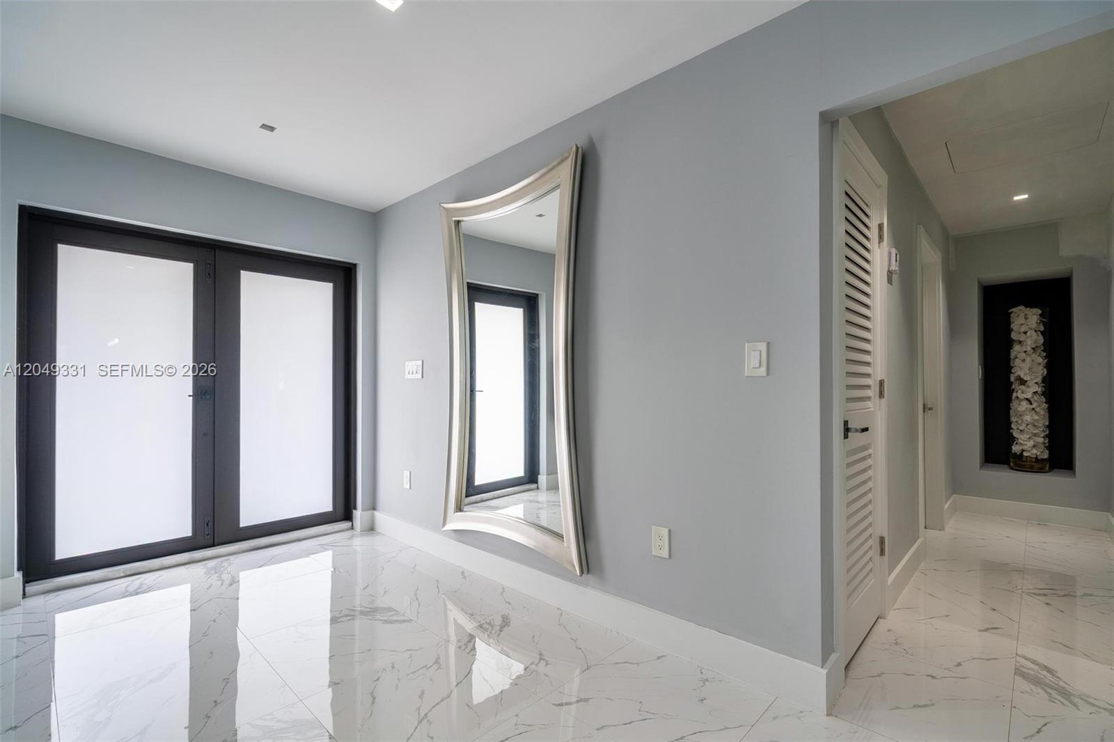A minimalist entryway features white marble floors, a large silver-framed mirror, and gray walls — 20221 SW 318th St, Homestead FL 33030, HOMESTEAD, FL