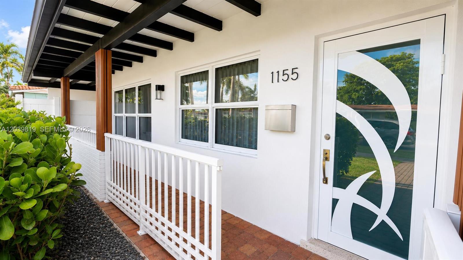 The exterior of a white house features a covered porch, a patterned glass door, and windows — 1155 Hayes St, Hollywood FL 33019, HOLLYWOOD, FL