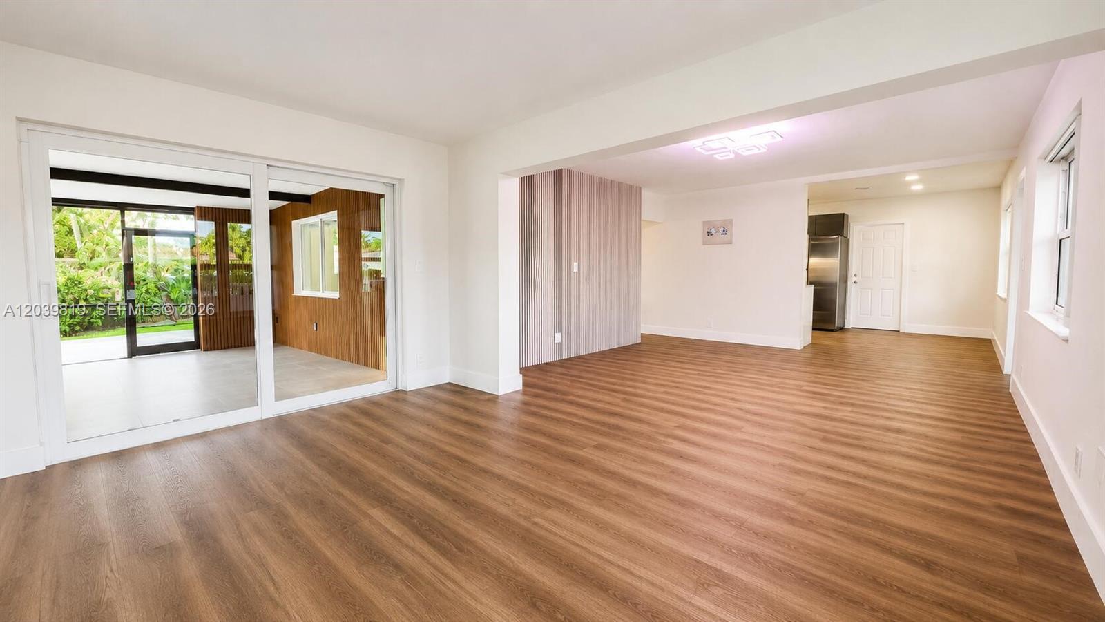 A bright living area features wood-look flooring, a slatted accent wall, and sliding glass doors — 1155 Hayes St, Hollywood FL 33019, HOLLYWOOD, FL