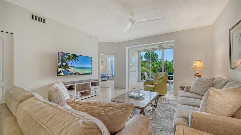 A living room features a beige sofa, a television, a coffee table, and a screened lanai — 8901 VERANDA WAY UNIT 111, SARASOTA, FL