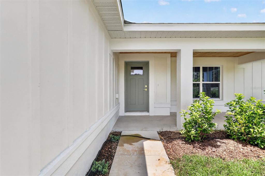 A concrete walkway leads to the front entrance of a white house with board-and-batten siding — 22 WALNUT COURSE, OCALA, FL
