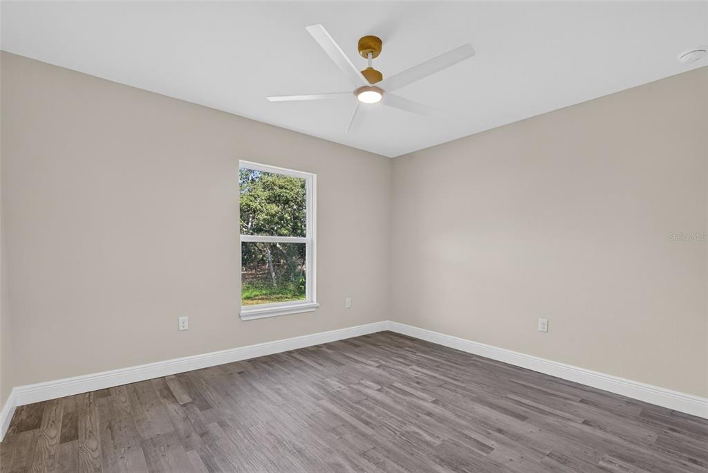 An empty bedroom features light beige walls, gray wood-look flooring, and a ceiling fan — 22 WALNUT COURSE, OCALA, FL