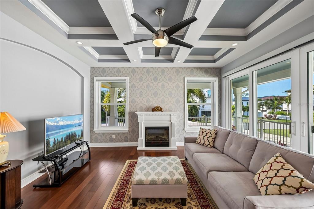 A living room features a coffered ceiling, a fireplace, patterned wallpaper, and a gray sofa — 8174 17TH AVENUE W, BRADENTON, FL
