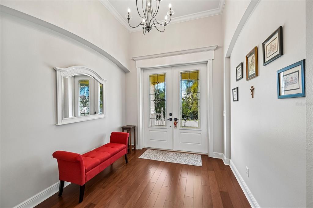 A bright entryway features a red bench, a mirror, and a chandelier over wood flooring — 8174 17TH AVENUE W, BRADENTON, FL