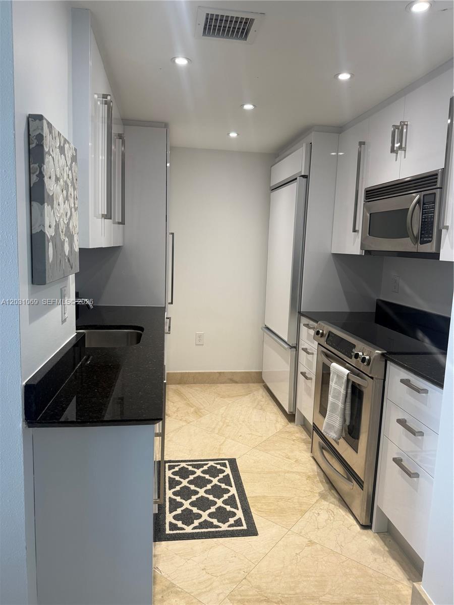 A galley kitchen features white cabinets, black countertops, stainless steel appliances, and tiled flooring — 10275 Collins Ave # 1221, Bal Harbour FL 33154, BAL HARBOUR, FL