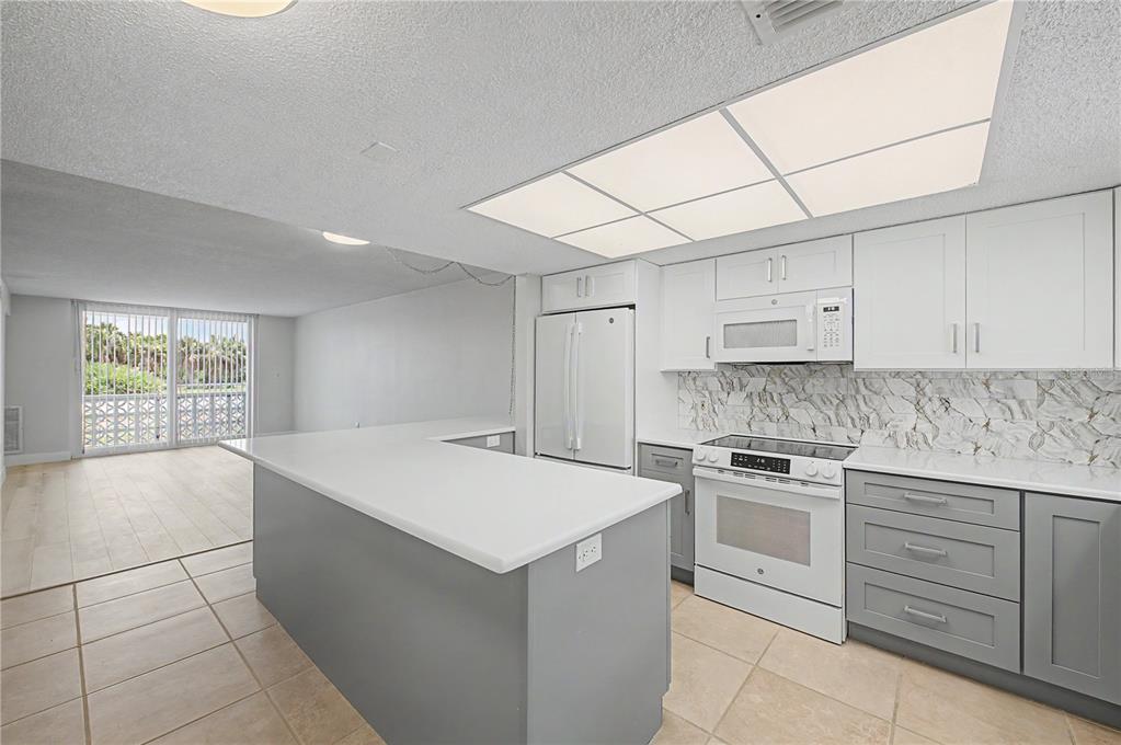 A kitchen with gray lower cabinets, white upper cabinets, and a white peninsula countertop — 9 FORBES PLACE UNIT 108, DUNEDIN, FL