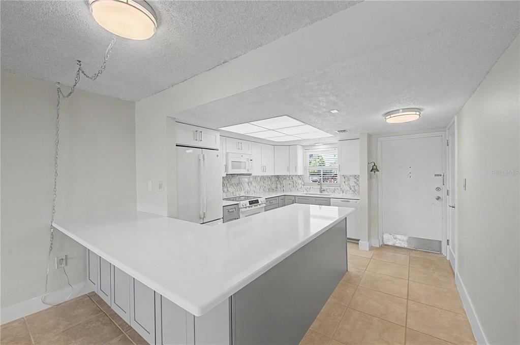 A kitchen features white countertops, gray lower cabinets, white upper cabinets, and tile flooring — 9 FORBES PLACE UNIT 108, DUNEDIN, FL