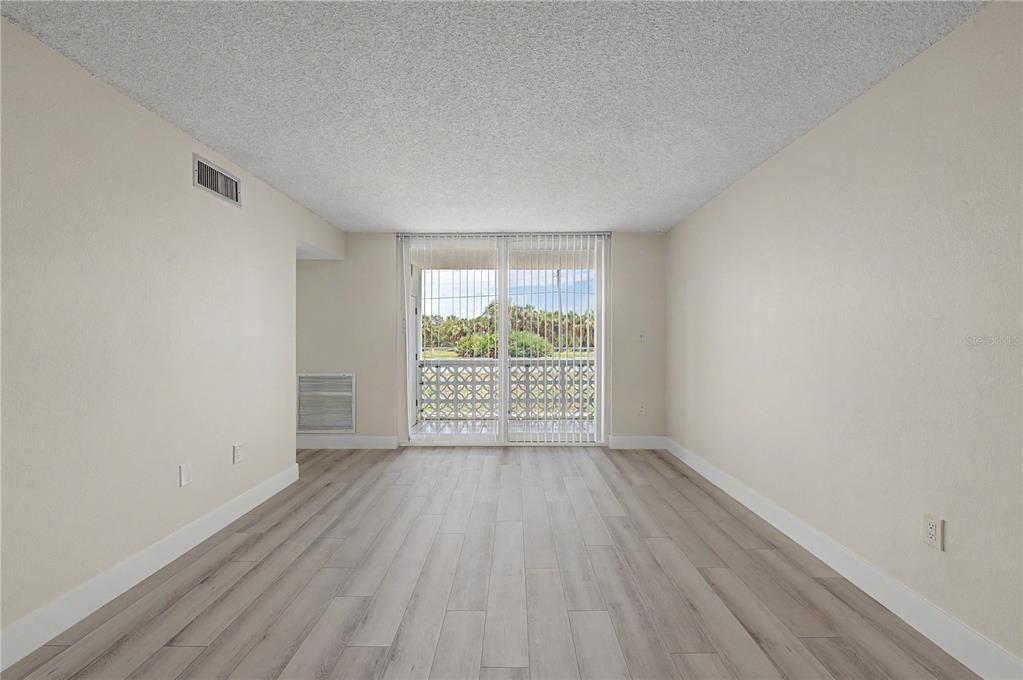 An empty room with light wood-look flooring, white walls, and a sliding glass balcony door — 9 FORBES PLACE UNIT 108, DUNEDIN, FL
