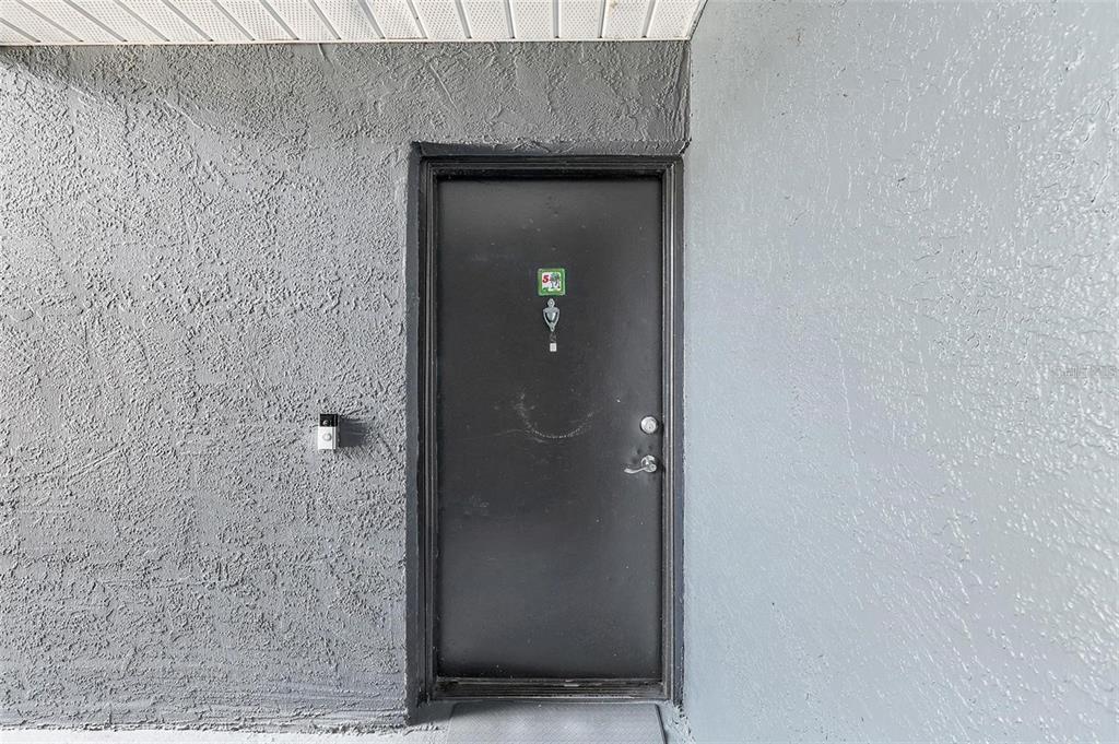 A black front door is set into a gray textured stucco wall under an overhang — 4252 PERSHING POINTE PLACE UNIT 5, ORLANDO, FL