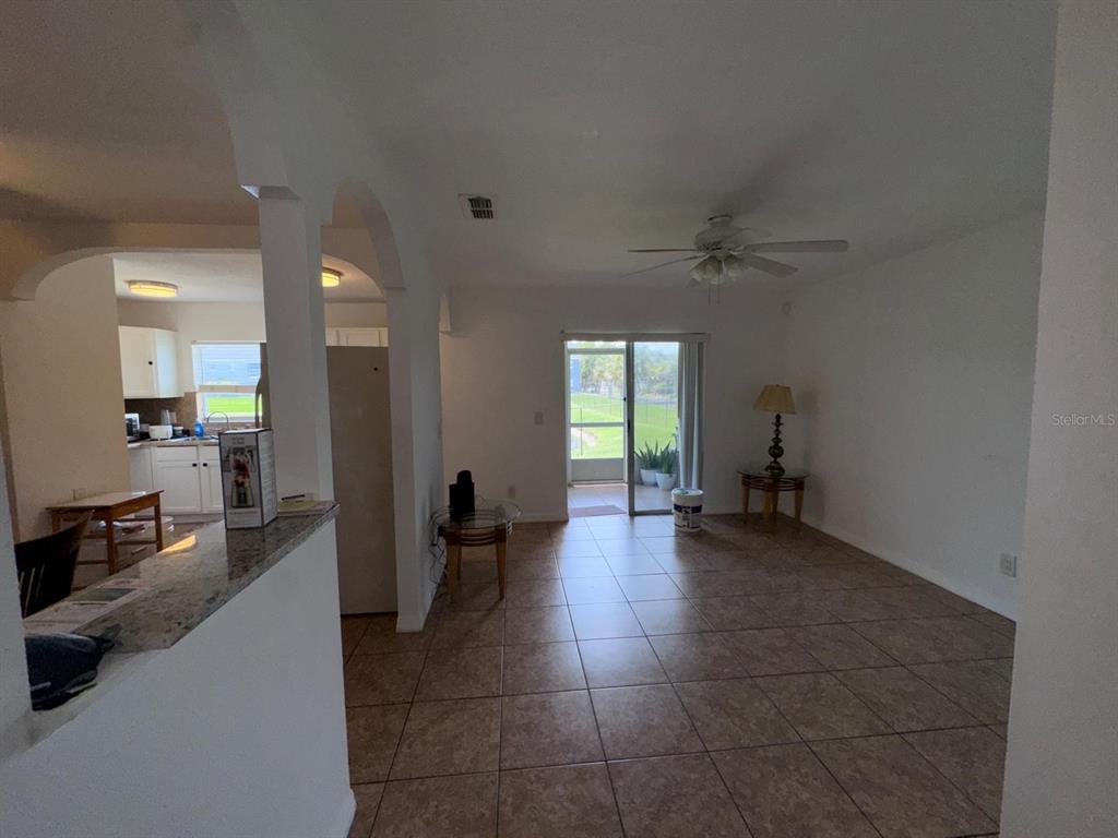 A living room with tile flooring leads to a sliding glass door and a kitchen — 4252 PERSHING POINTE PLACE UNIT 5, ORLANDO, FL