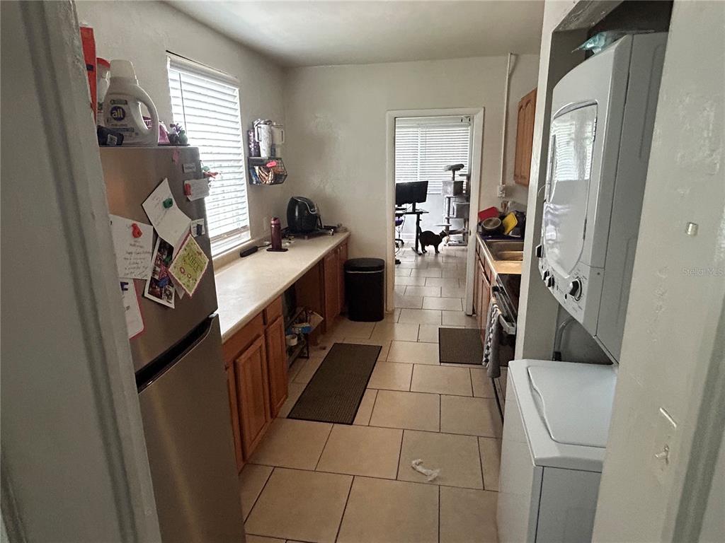 A galley-style kitchen features light wood cabinets, tile flooring, and a stacked washer and dryer — 1220 NW 31 AVENUE, GAINESVILLE, FL