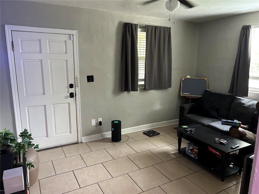 A living room features light tile flooring, gray walls, a white door, and a dark sofa — 1220 NW 31 AVENUE, GAINESVILLE, FL