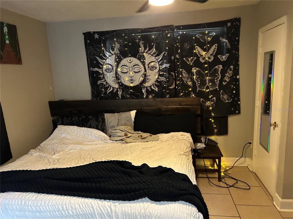 A bedroom features a bed with a dark headboard, a sun-themed tapestry, and tile flooring — 1220 NW 31 AVENUE, GAINESVILLE, FL