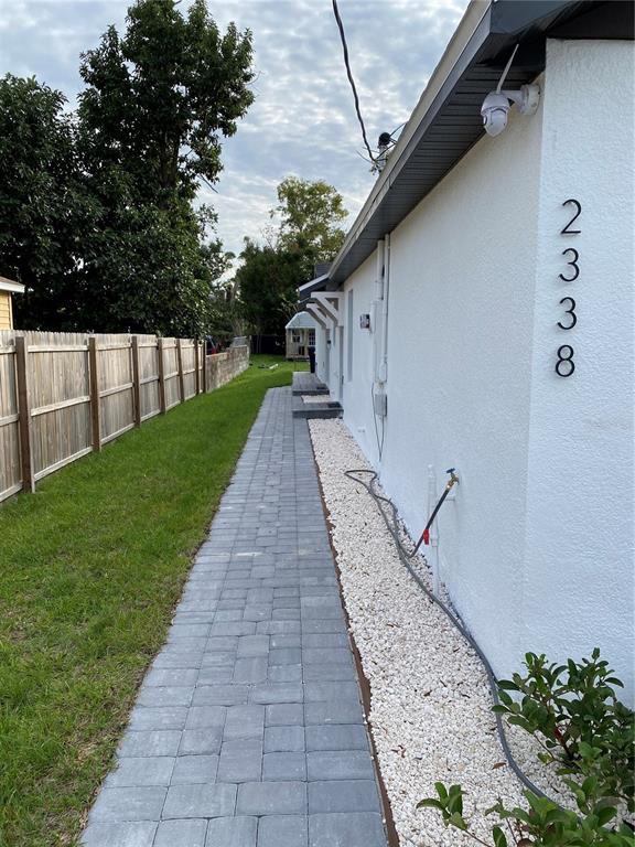 A paved walkway runs alongside a white house with a gravel bed and wooden fence — 2336-2338 E JERSEY AVENUE, ORLANDO, FL