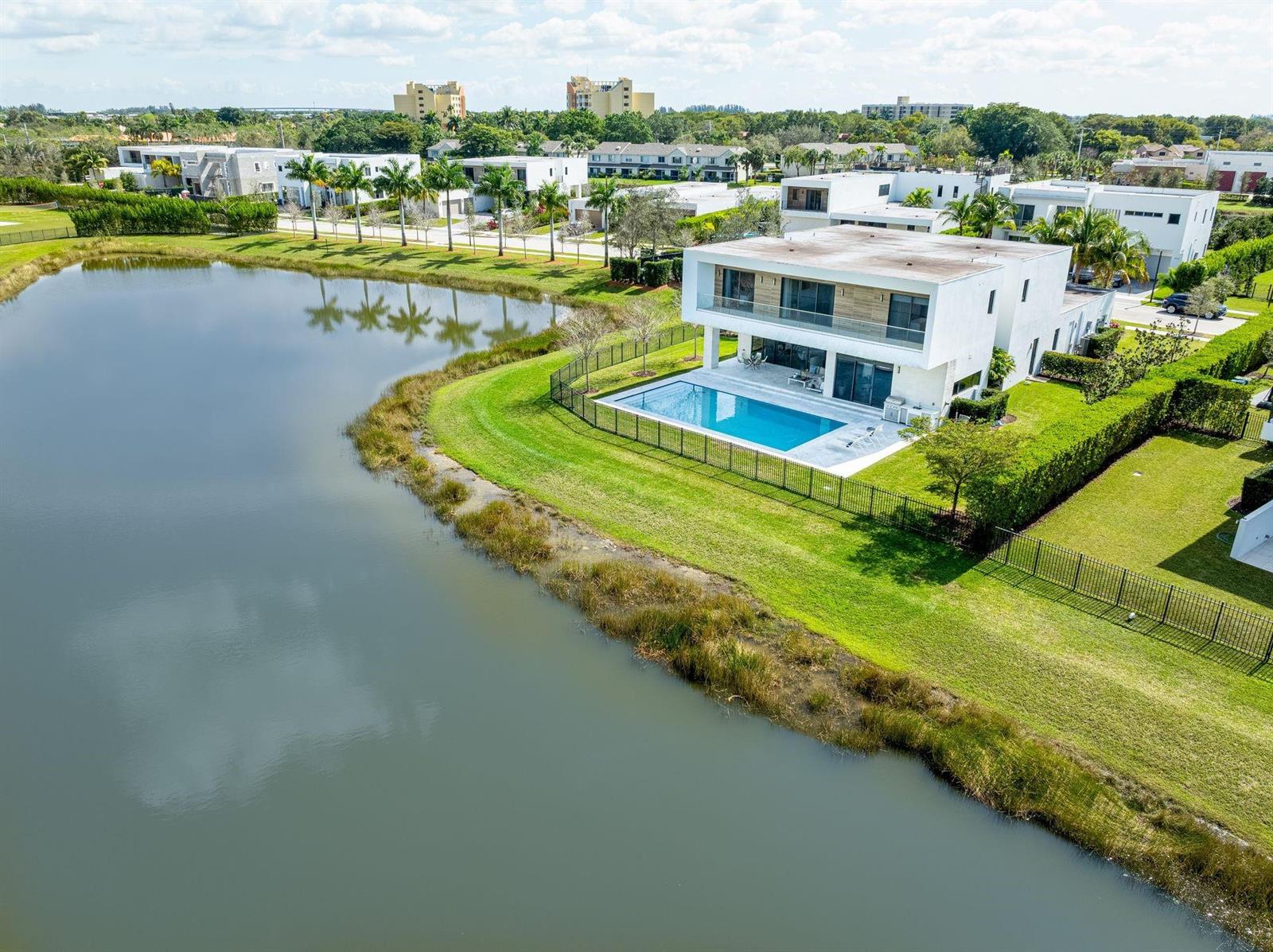 An aerial view of a modern white house with a pool beside a lake — 16553 Botaniko Drive S, Weston FL 33326, WESTON, FL