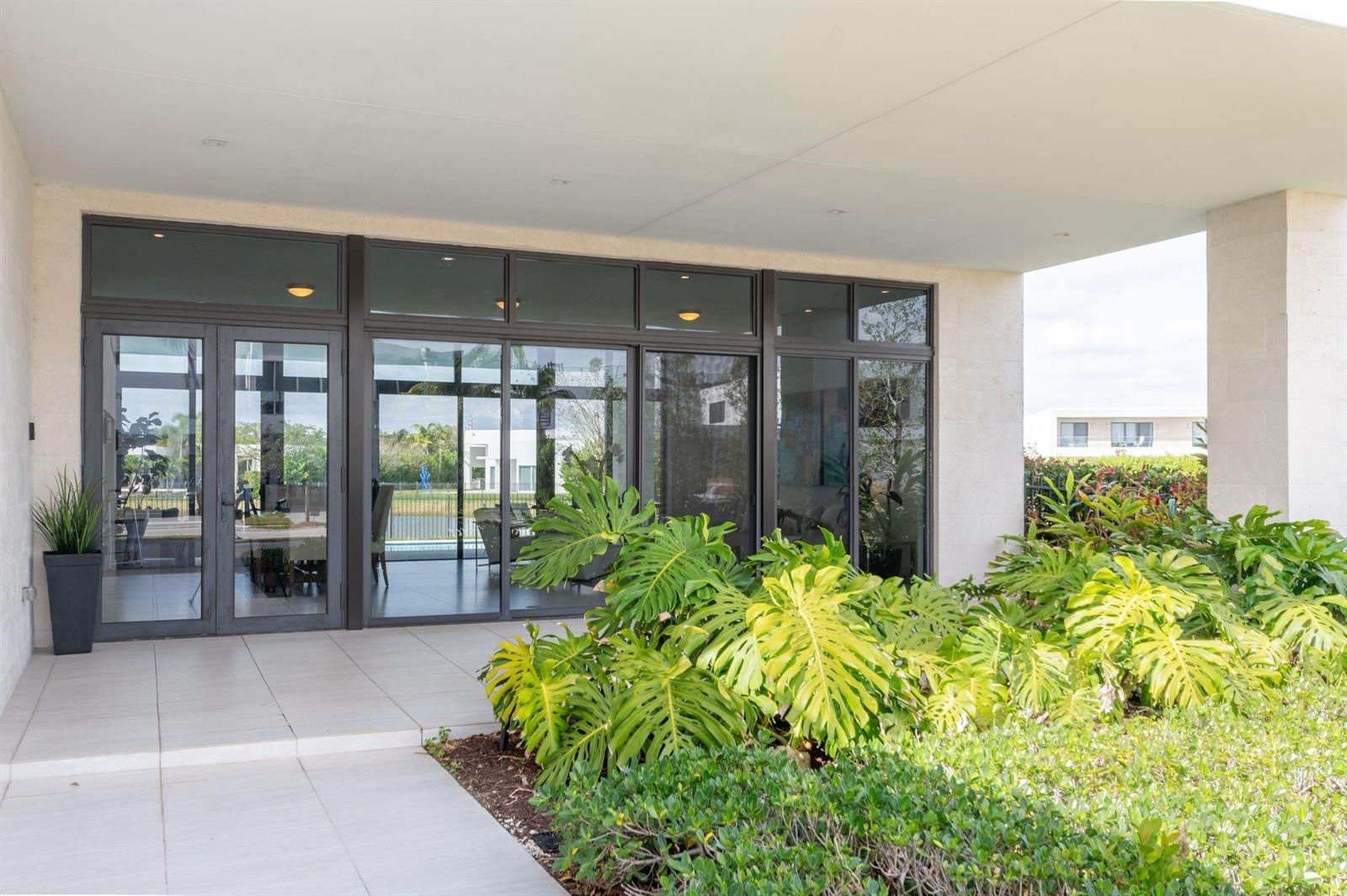 A covered patio with large glass doors and windows overlooks a garden and pool area — 16553 Botaniko Drive S, Weston FL 33326, WESTON, FL