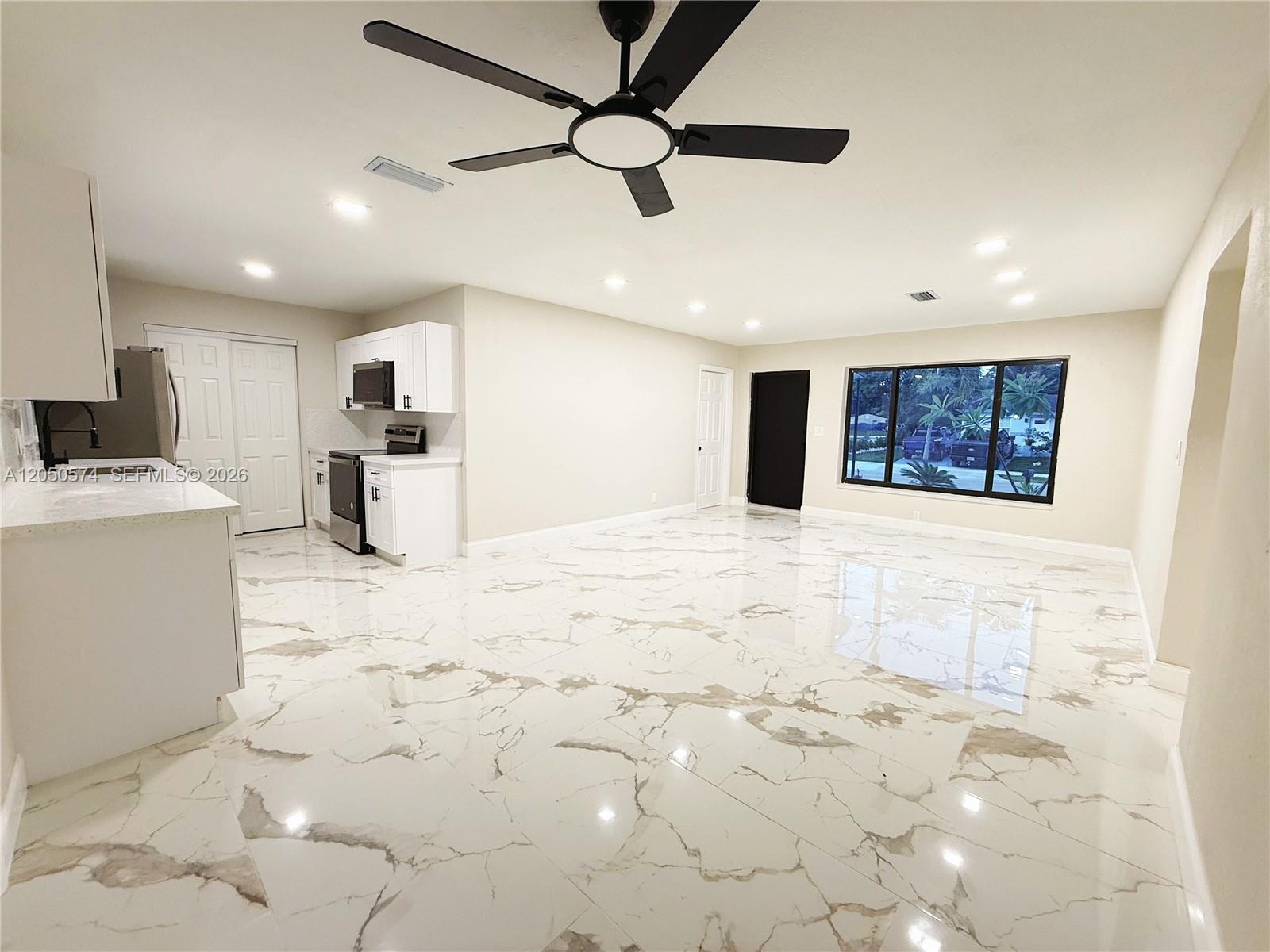 An open-concept kitchen and living area features white marble-look tile floors and a ceiling fan — 2401 SW 50th Ter, Plantation FL 33317, PLANTATION, FL