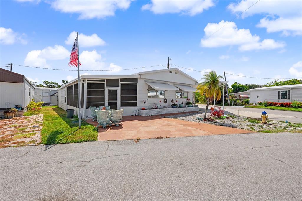 A white mobile home with a screened porch, patio, and American flag stands outdoors — 6523 KANSAS STREET, BRADENTON, FL