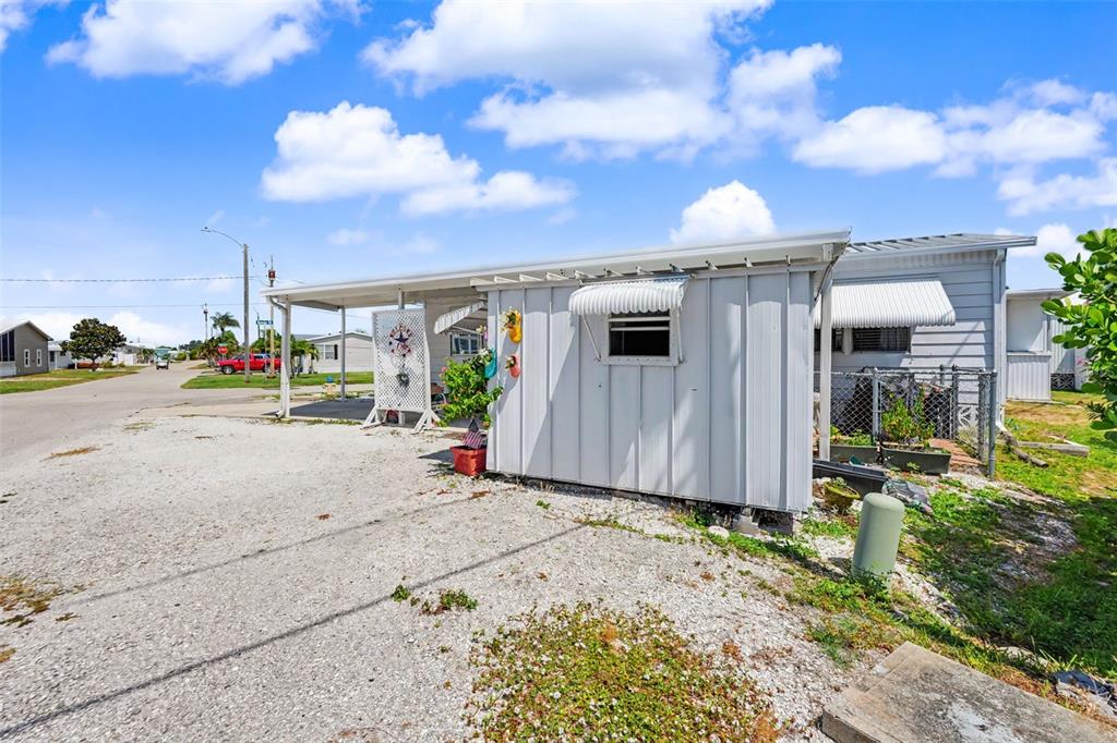 A white mobile home with a gravel driveway and a covered carport under a blue sky — 6523 KANSAS STREET, BRADENTON, FL