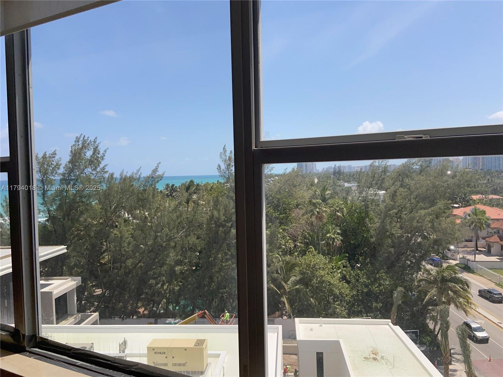 An elevated view through a window shows trees, a road, and the distant ocean — 3180 S Ocean Dr # 716, Hallandale Beach FL 33009, HALLANDALE BEACH, FL