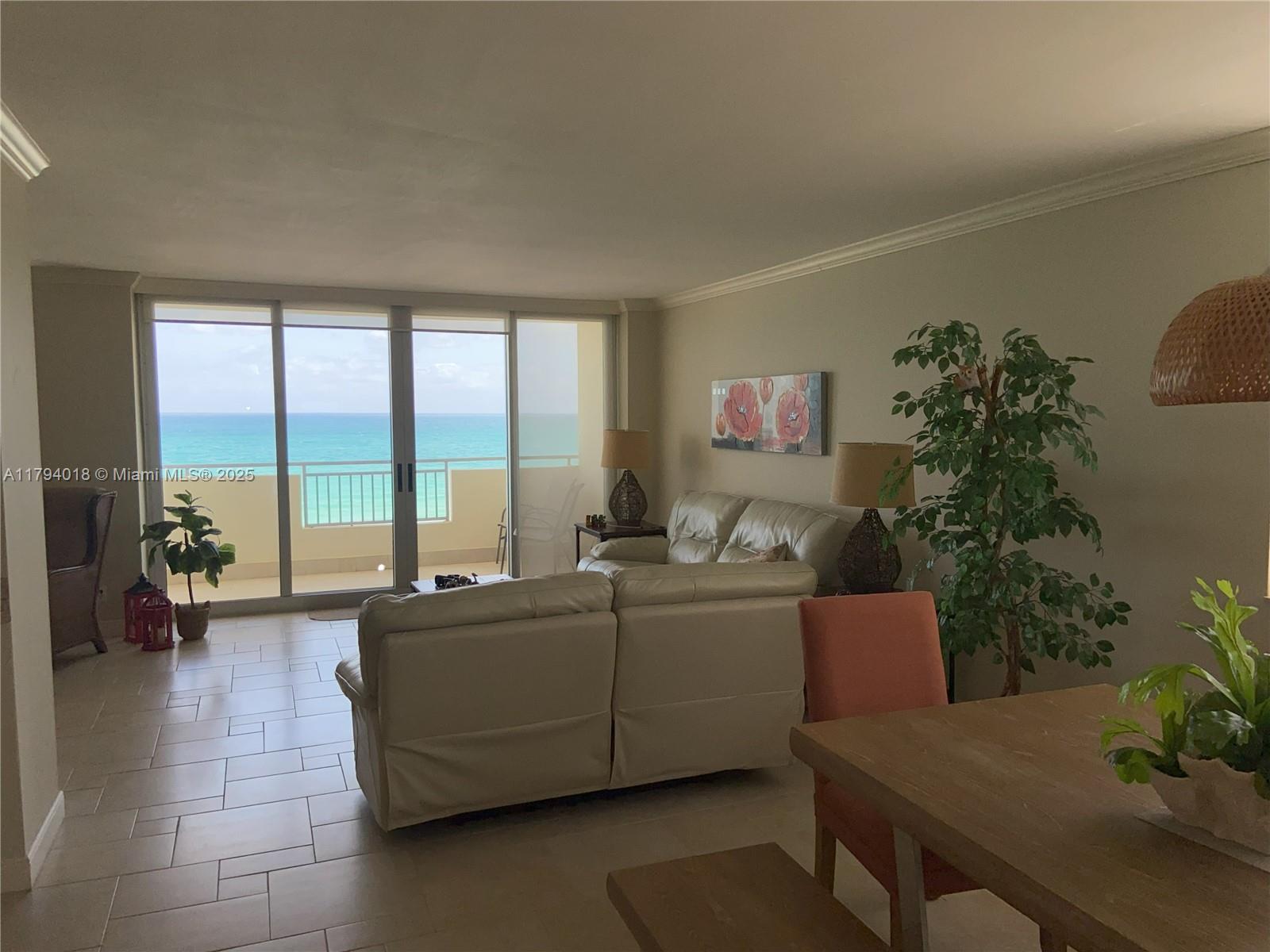 A living room with tile floors features a leather sofa and a balcony overlooking the ocean — 3180 S Ocean Dr # 716, Hallandale Beach FL 33009, HALLANDALE BEACH, FL