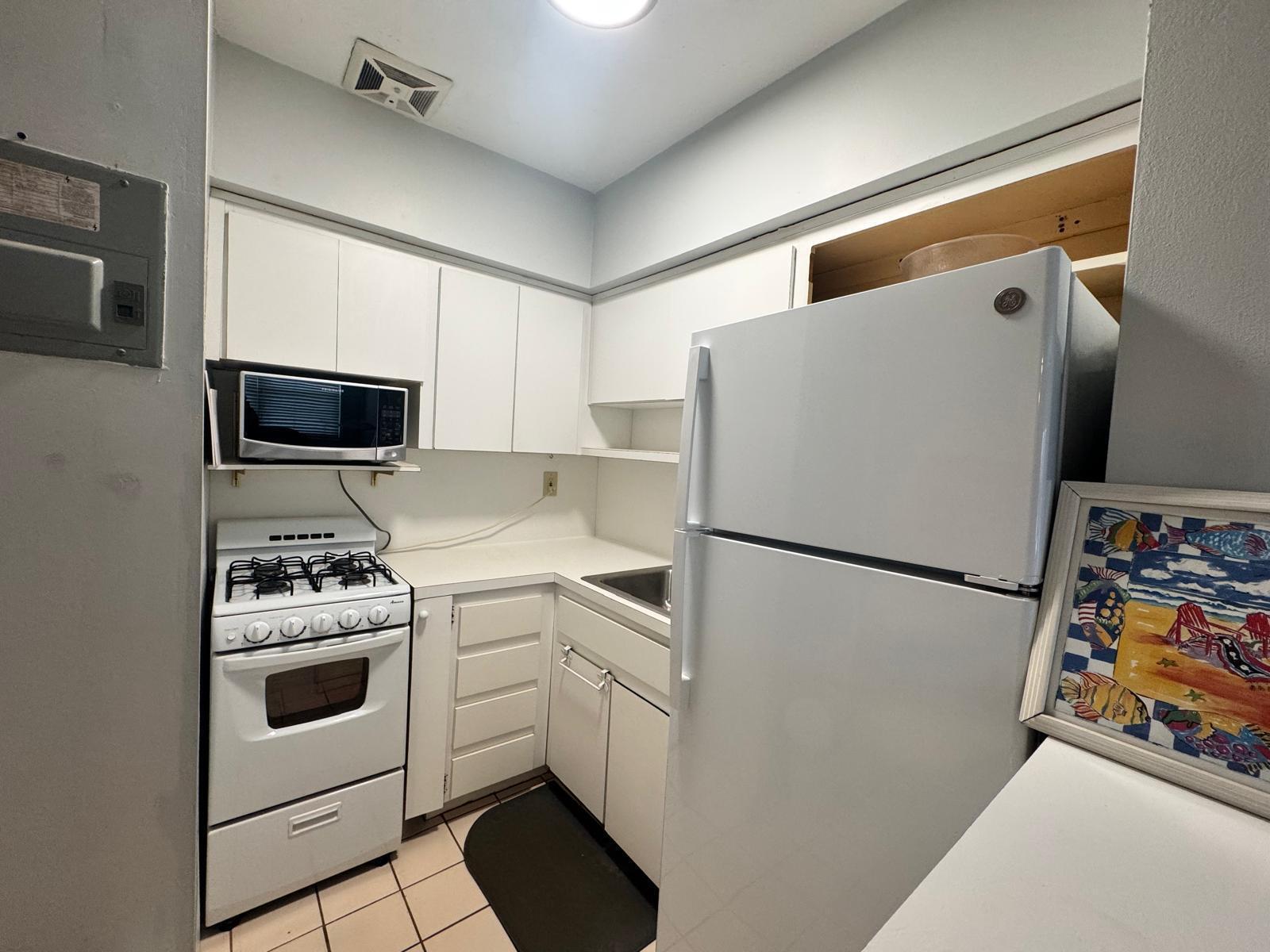 A small kitchen features white cabinets, a gas stove, a refrigerator, and tiled flooring — 2001 S Ocean Drive # 46, Hallandale Beach FL 33009, HALLANDALE BEACH, FL