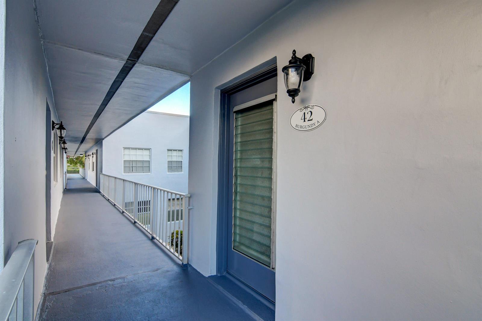An outdoor walkway leads past a blue door with a numbered plaque and wall lamp — 42 Burgundy A, Delray Beach FL 33484, DELRAY BEACH, FL