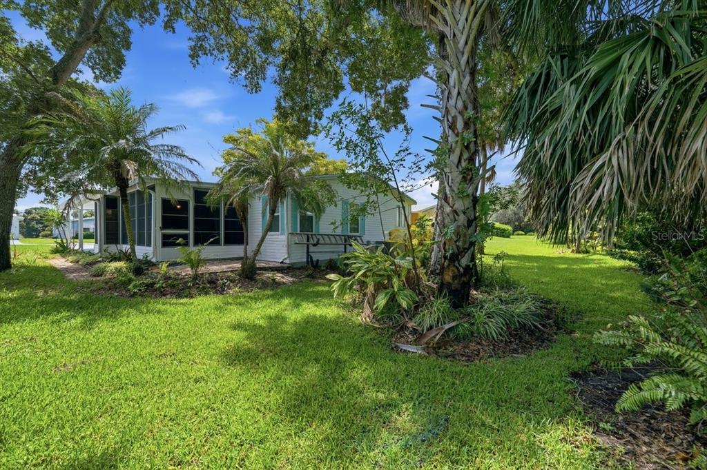 A white mobile home with a screened-in porch sits on a grassy lot with trees — 304 PORTSIDE LANE, EDGEWATER, FL